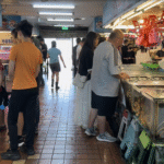 竹圍漁港展售中心一樓，兩側魚販擺攤，人們在攤位前挑選海鮮